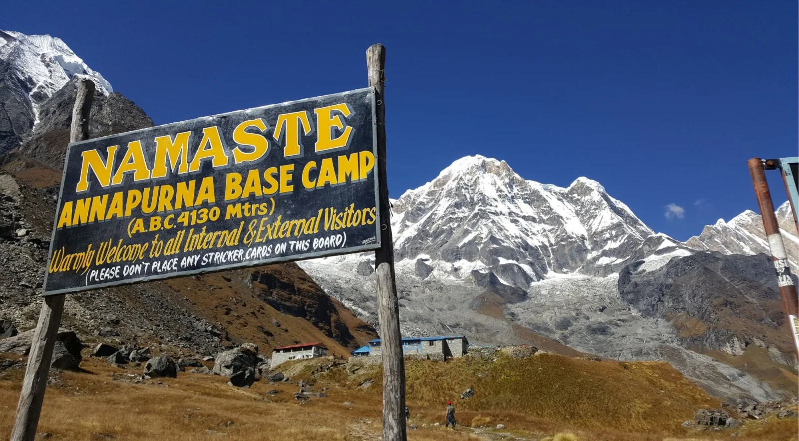 Close-up of the Namaste Annapurna Base Camp 4,130 m sign with Annapurna South and the base camp lodges behind