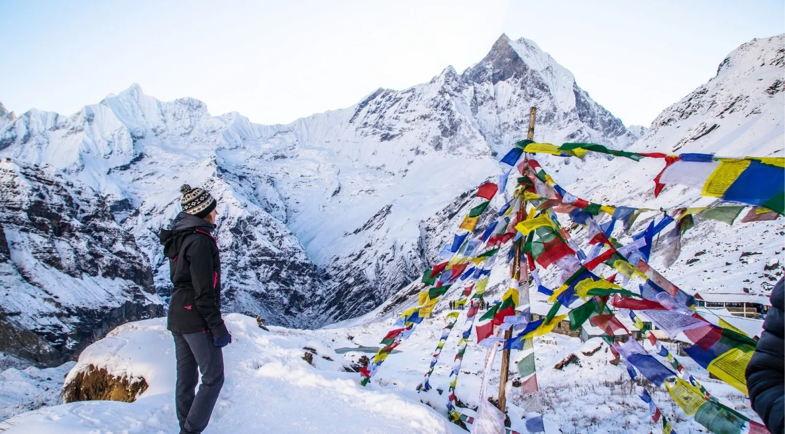 Trekker in a wool hat standing in deep snow at Annapurna Base Camp looking across at Machhapuchhre