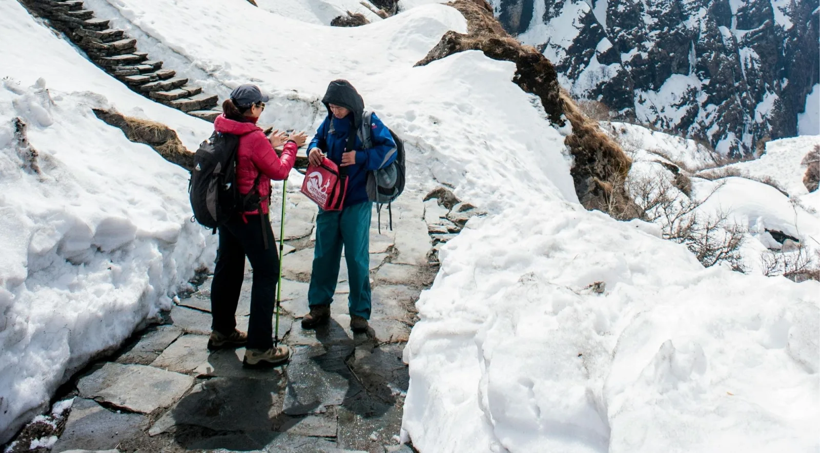Two trekkers and a guide pausing on a snow-covered stone staircase on the trail to the Sanctuary
