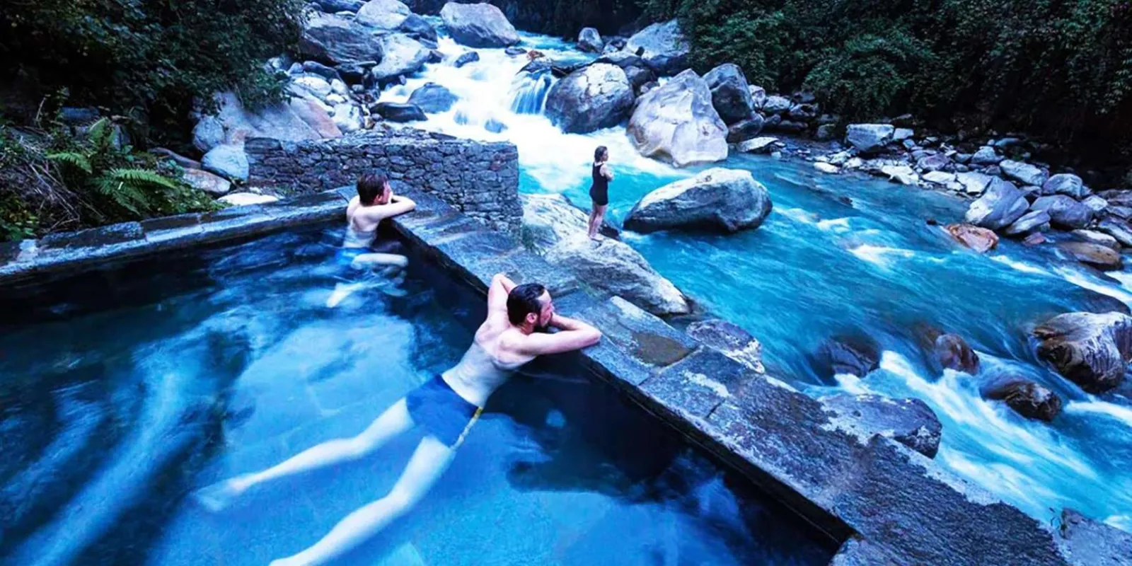 Trekkers soaking in the stone-walled Jhinu Danda hot spring pools beside the turquoise Modi Khola