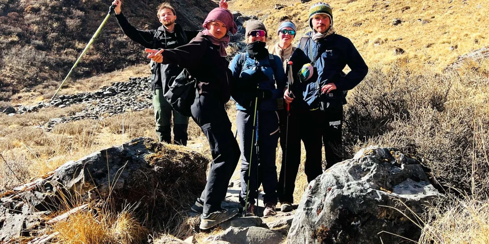 Guide pointing out a peak to trekkers standing on boulders among golden autumn grass