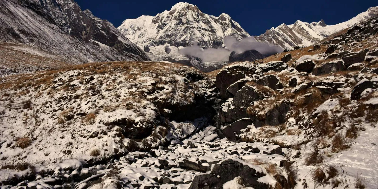 Annapurna South rising above a snow-dusted moraine and golden grass under a deep blue sky