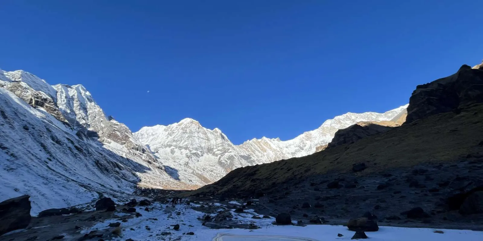 The Annapurna Sanctuary amphitheatre under a clear blue sky with trekkers crossing the snowfield